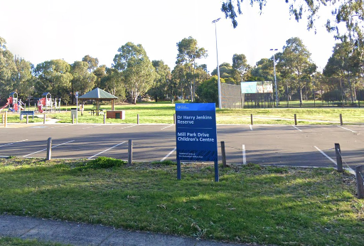 A park area featuring a playground, picnic shelter, and sports courts, with a sign for Dr. Harry Jenkins Reserve and Mill Park Drive Children's Centre.